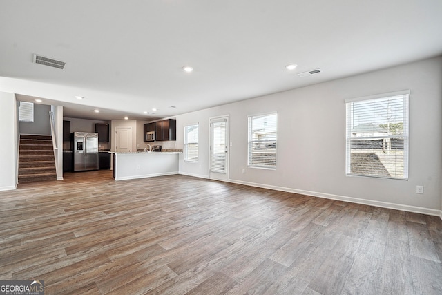 unfurnished living room featuring stairway, light wood-type flooring, visible vents, and recessed lighting