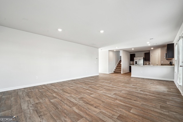 unfurnished living room with recessed lighting, wood finished floors, and stairs