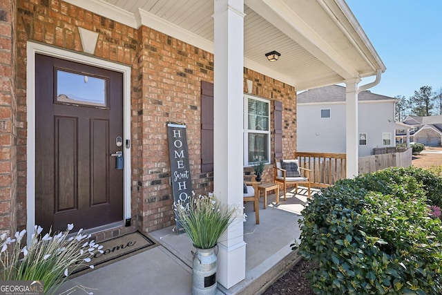 view of exterior entry featuring a porch and brick siding