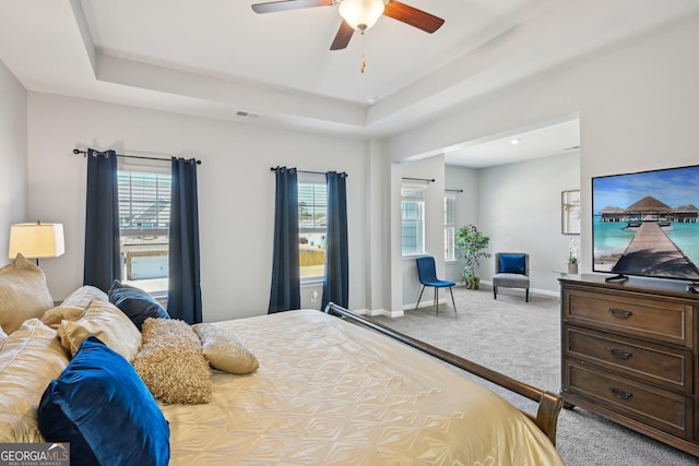 carpeted bedroom featuring a tray ceiling, visible vents, and multiple windows