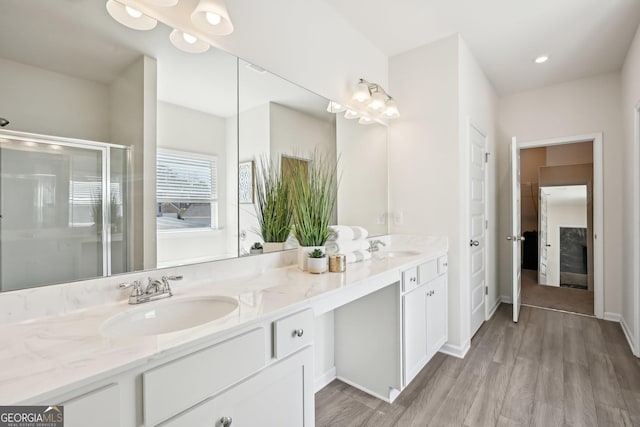 full bath featuring double vanity, a stall shower, a sink, and wood finished floors