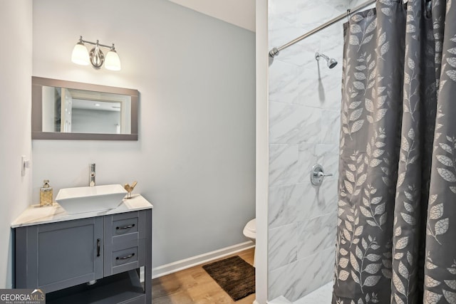 full bath with baseboards, tiled shower, toilet, wood finished floors, and vanity