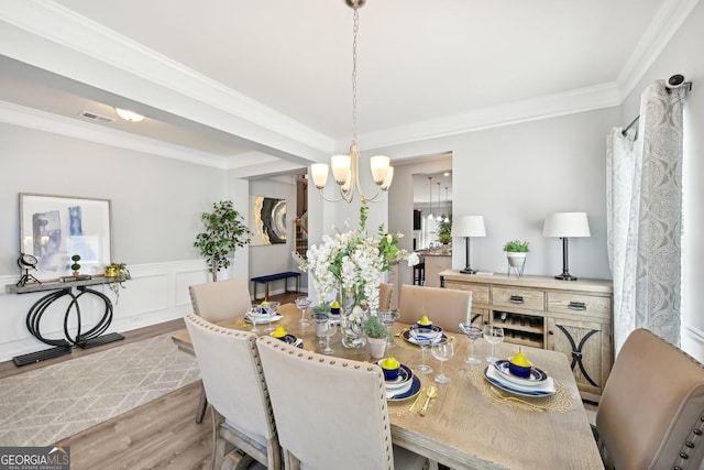 dining room featuring ornamental molding, wainscoting, visible vents, and wood finished floors