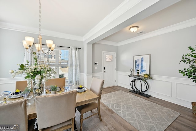 dining space featuring a chandelier, a wainscoted wall, visible vents, and wood finished floors