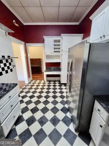 kitchen featuring a paneled ceiling, white cabinets, freestanding refrigerator, light floors, and dark countertops