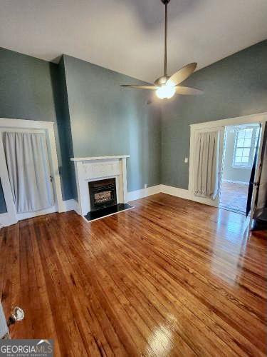 unfurnished living room with a fireplace, wood finished floors, a ceiling fan, and baseboards