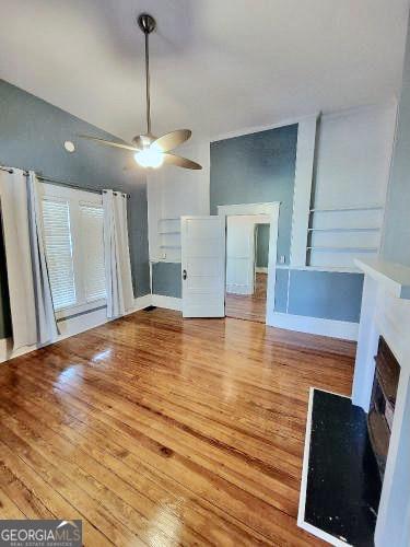 unfurnished living room with ceiling fan, a fireplace, wood finished floors, baseboards, and vaulted ceiling