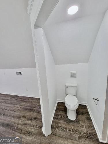 bathroom featuring lofted ceiling, toilet, wood finished floors, visible vents, and baseboards