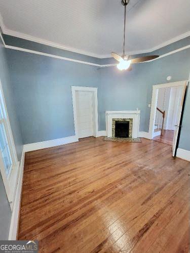 unfurnished living room with baseboards, ornamental molding, wood finished floors, and a stone fireplace