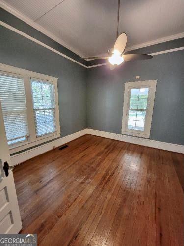 unfurnished room with baseboards, ornamental molding, ceiling fan, and dark wood-type flooring