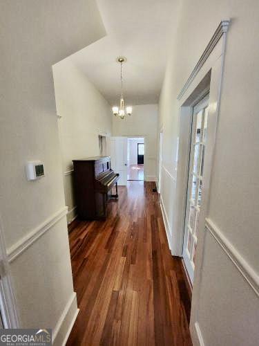 hallway with a wainscoted wall, a decorative wall, dark wood finished floors, and an inviting chandelier