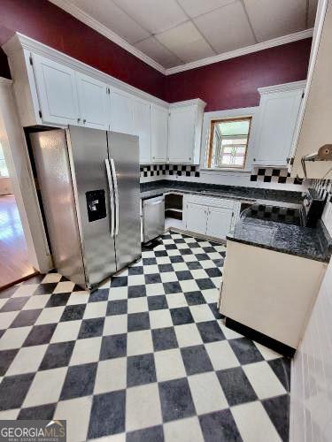 kitchen featuring dark countertops, dark floors, appliances with stainless steel finishes, crown molding, and white cabinetry