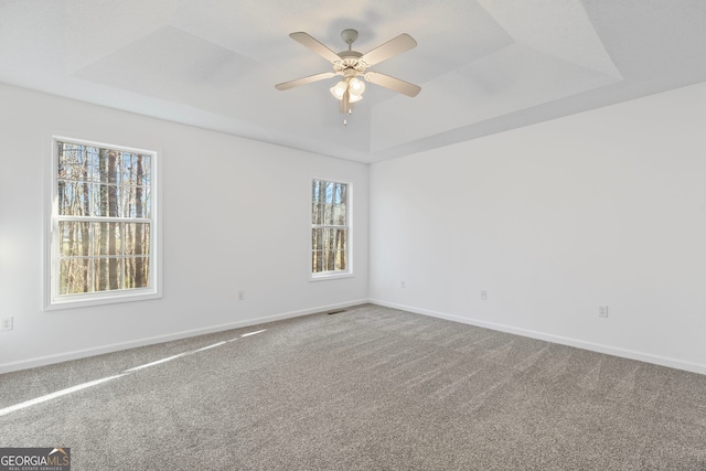 carpeted spare room featuring baseboards, a raised ceiling, and a ceiling fan