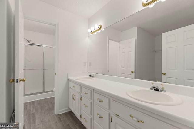 bathroom featuring a sink, wood finished floors, a stall shower, and double vanity