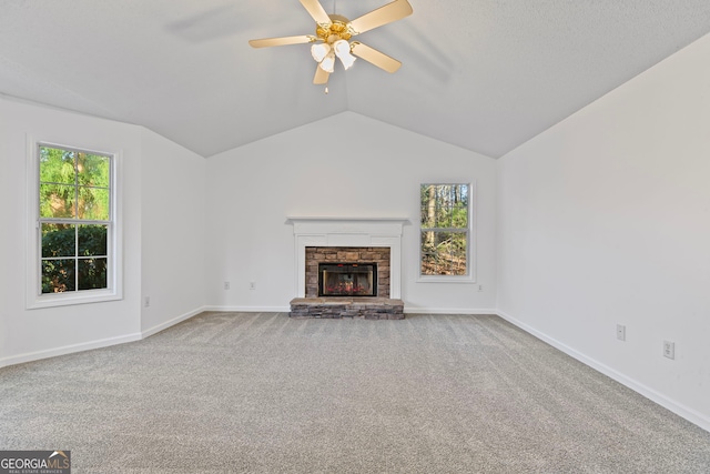 unfurnished living room with carpet flooring, a stone fireplace, lofted ceiling, and a ceiling fan