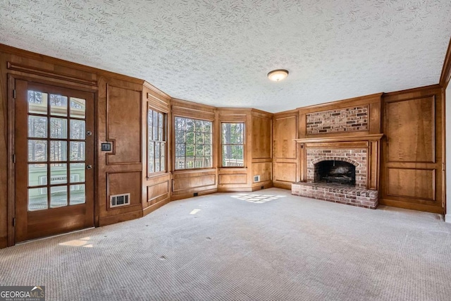 unfurnished living room with a textured ceiling, a decorative wall, carpet flooring, visible vents, and a brick fireplace