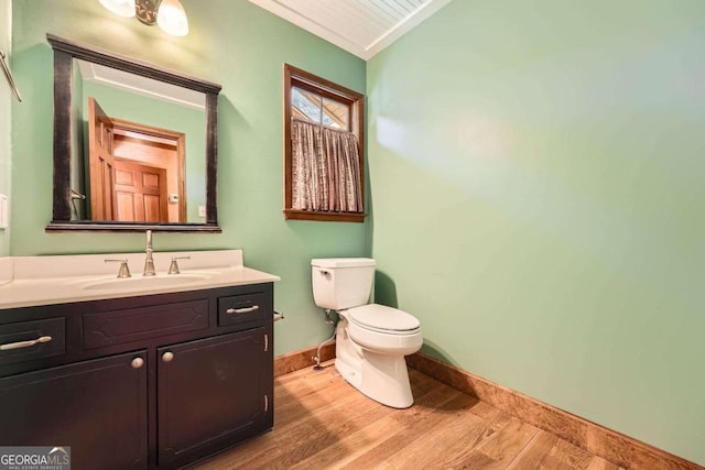 half bath featuring toilet, vaulted ceiling, vanity, wood finished floors, and baseboards