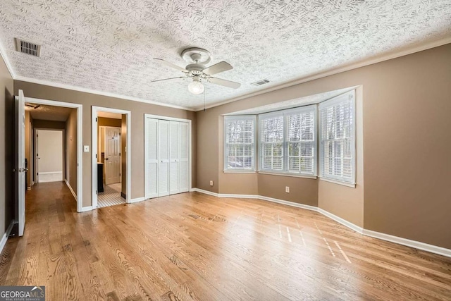 unfurnished bedroom featuring light wood finished floors, a closet, baseboards, and crown molding