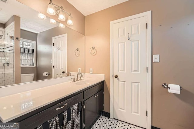 bathroom featuring toilet, tiled shower, and vanity