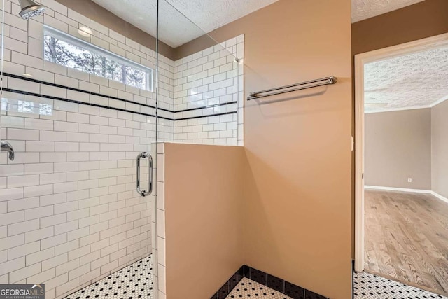 full bath featuring a stall shower, baseboards, a textured ceiling, and wood finished floors