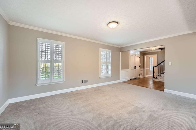 spare room with visible vents, stairs, dark carpet, plenty of natural light, and crown molding