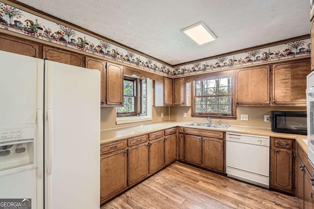 kitchen featuring brown cabinets, light wood finished floors, a sink, a textured ceiling, and white appliances