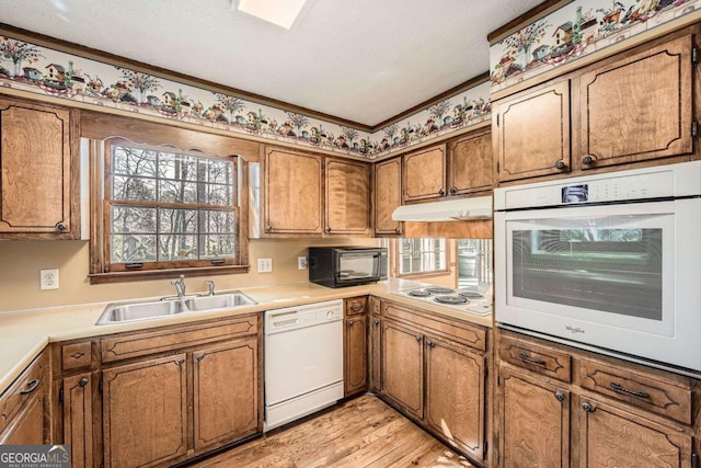 kitchen featuring white appliances, light wood-style flooring, brown cabinets, under cabinet range hood, and a sink