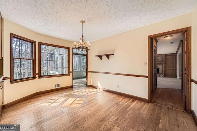 unfurnished dining area with a textured ceiling, hardwood / wood-style flooring, a notable chandelier, visible vents, and a brick fireplace