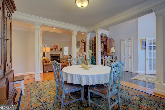 dining space featuring baseboards, ornamental molding, wood finished floors, ornate columns, and a fireplace