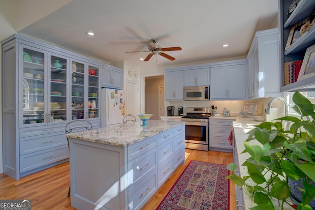 kitchen featuring light stone counters, light wood-style flooring, stainless steel appliances, a center island, and glass insert cabinets