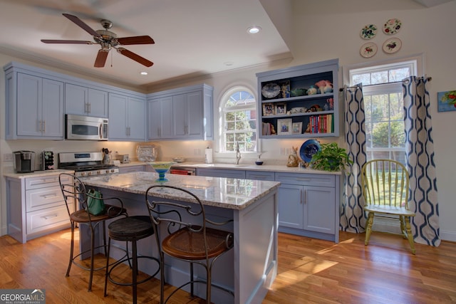 kitchen with light stone counters, a center island, stainless steel appliances, light wood-style floors, and a kitchen breakfast bar