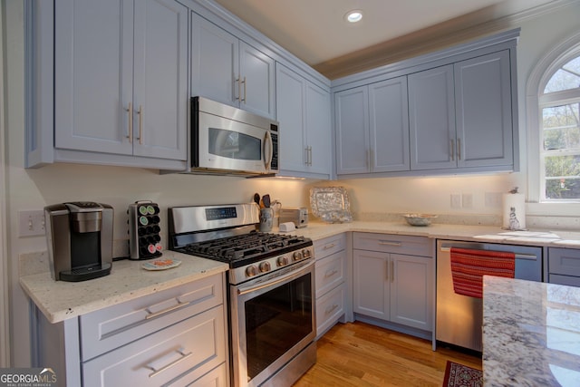 kitchen with stainless steel appliances, gray cabinets, light wood-style flooring, and light stone countertops