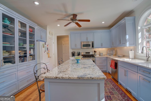 kitchen featuring light stone countertops, appliances with stainless steel finishes, a sink, and a center island