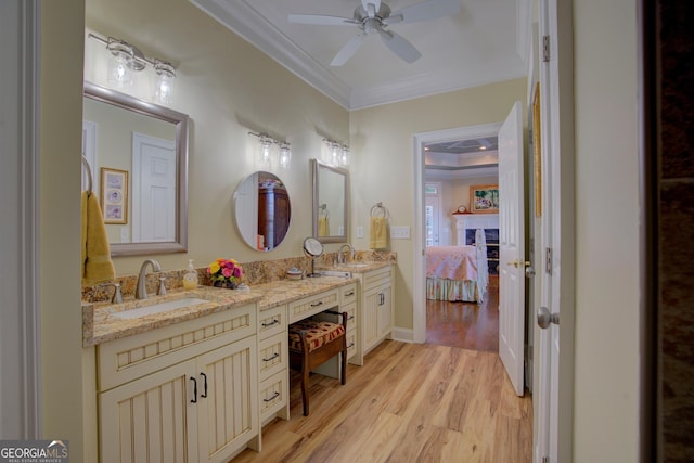 ensuite bathroom with double vanity, ceiling fan, wood finished floors, crown molding, and a sink