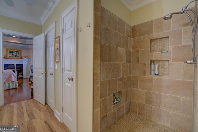 bathroom featuring a fireplace, a tile shower, and crown molding