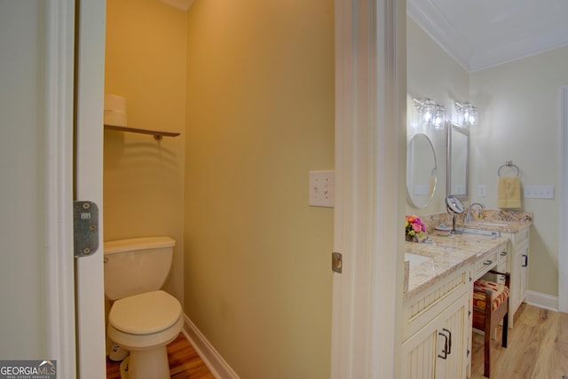 bathroom with double vanity, toilet, ornamental molding, a sink, and wood finished floors