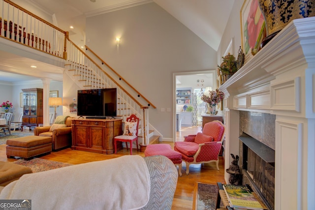 living room with stairway, a high ceiling, crown molding, light wood-style floors, and a fireplace