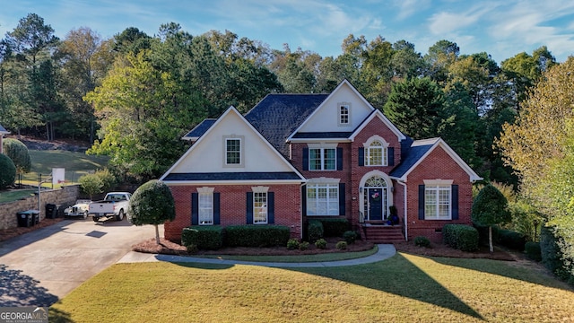 traditional-style home with a shingled roof, a front yard, concrete driveway, and brick siding