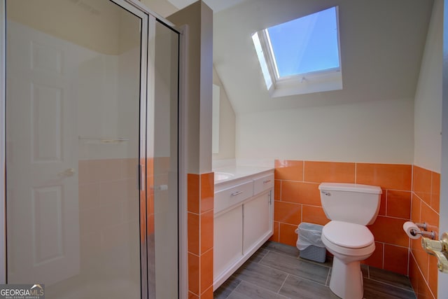 bathroom featuring vaulted ceiling with skylight, toilet, vanity, tile walls, and a shower stall