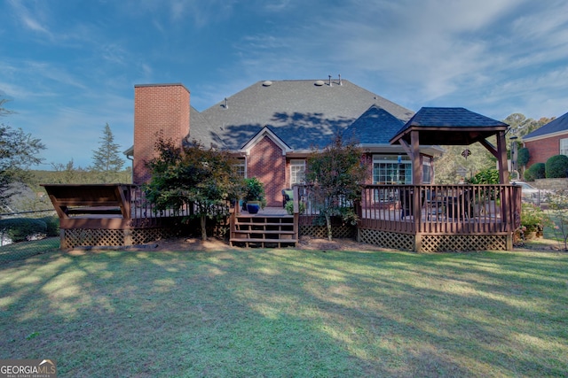 rear view of property with a shingled roof, a lawn, a chimney, a deck, and brick siding