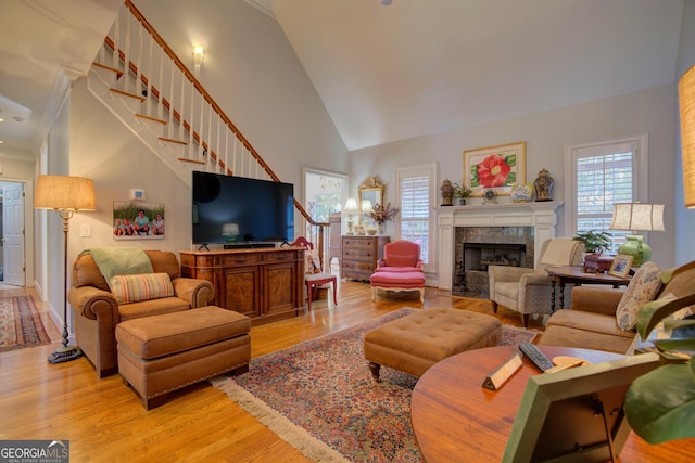 living room with light wood-type flooring, stairway, a premium fireplace, and high vaulted ceiling