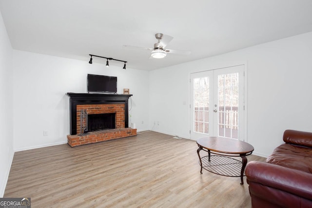 living room with a ceiling fan, wood finished floors, french doors, baseboards, and a brick fireplace