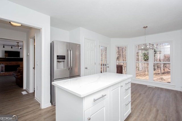 kitchen featuring stainless steel fridge, white cabinets, light wood-type flooring, and light stone countertops