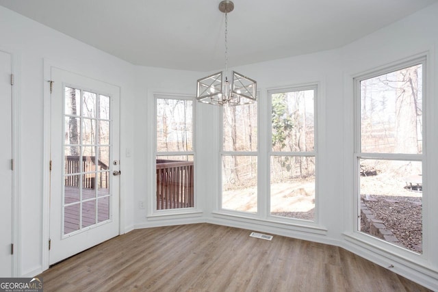 unfurnished dining area with an inviting chandelier, wood finished floors, and visible vents