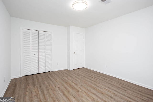 unfurnished bedroom with a closet, visible vents, baseboards, and wood finished floors