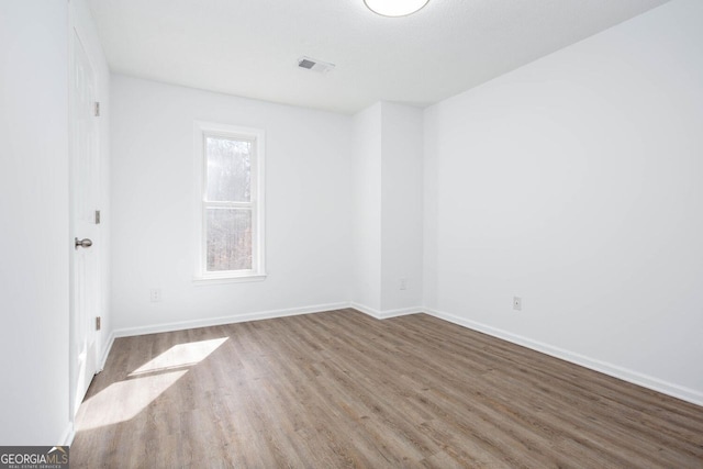 unfurnished room featuring visible vents, wood finished floors, and baseboards