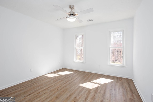 spare room featuring a wealth of natural light, visible vents, wood finished floors, and a ceiling fan