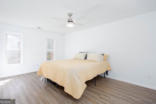 bedroom featuring ceiling fan, visible vents, baseboards, and wood finished floors