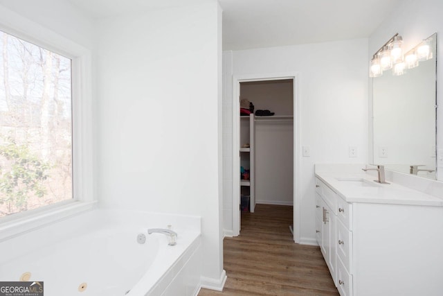 full bath featuring a walk in closet, baseboards, wood finished floors, a bath, and vanity