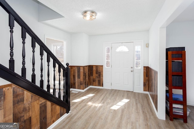 foyer featuring wood finished floors, a wainscoted wall, stairs, wood walls, and a textured ceiling